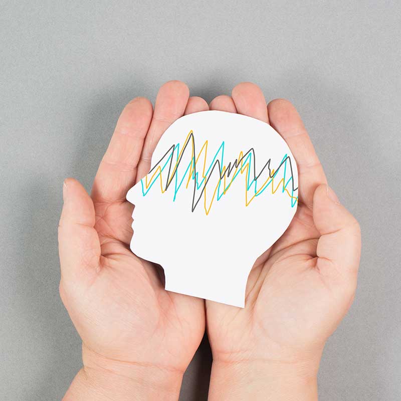 Two hands holding a cutout of a head made of white paper. A zig zag pattern appears in multiple colours on the head.